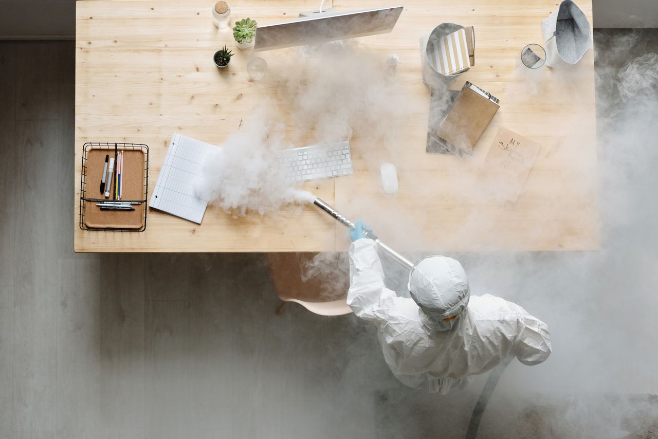 hero-img-02 An individual disinfects a workspace using fumigation, wearing full protective gear for safety.